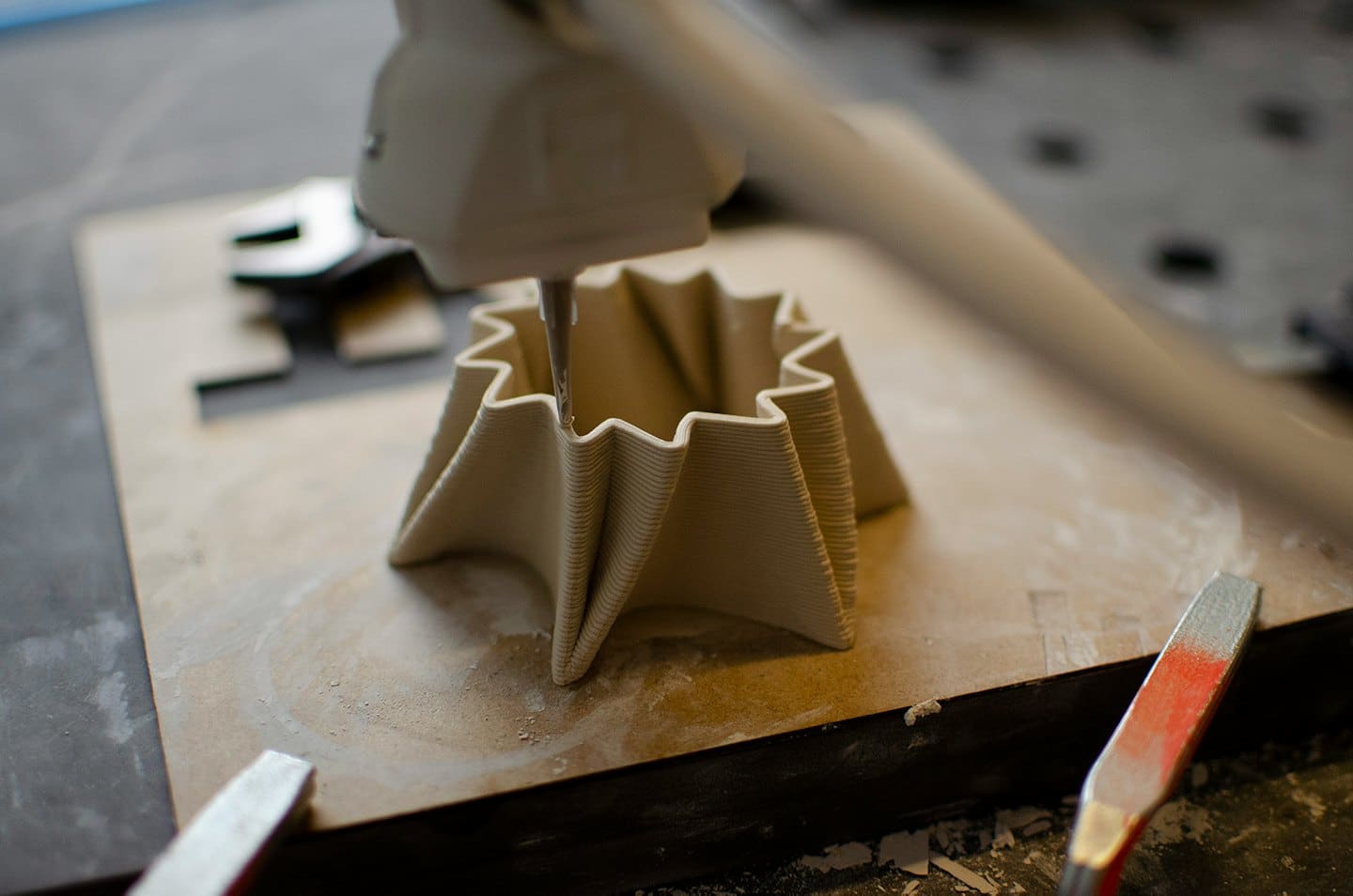 3D printer extruding a wavy ceramic object layer by layer.